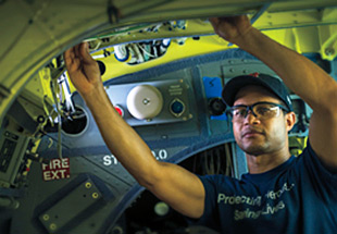 Mechanic in safety glasses and bump cap works on aircraft.